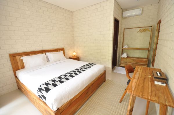 Cozy minimalist bedroom with wooden king bed, white brick walls, desk, and tropical accents. - Bali Villas